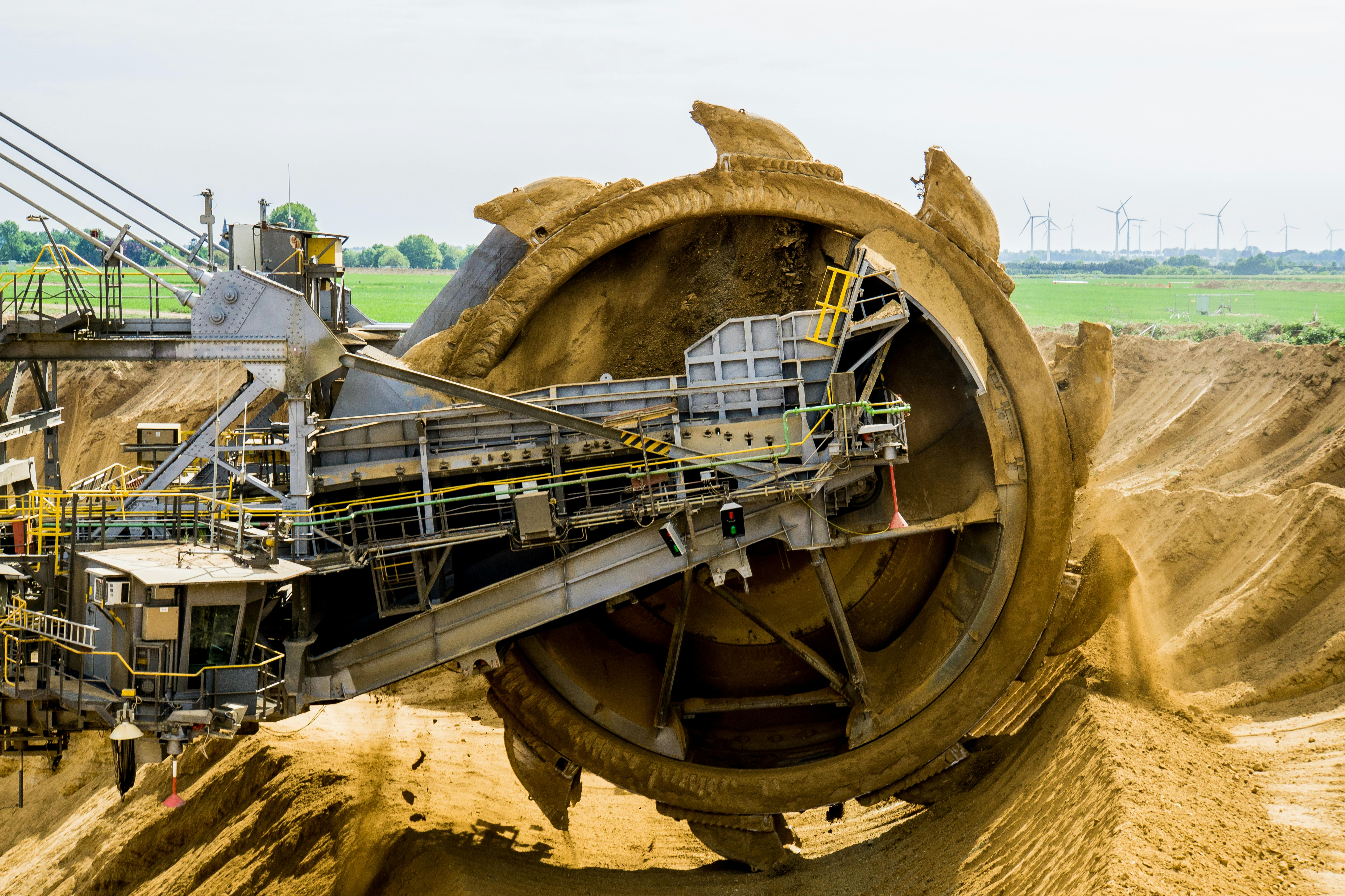 Bucket-wheel mining machine cutting through a sand stockpile with conveyors and field equipment