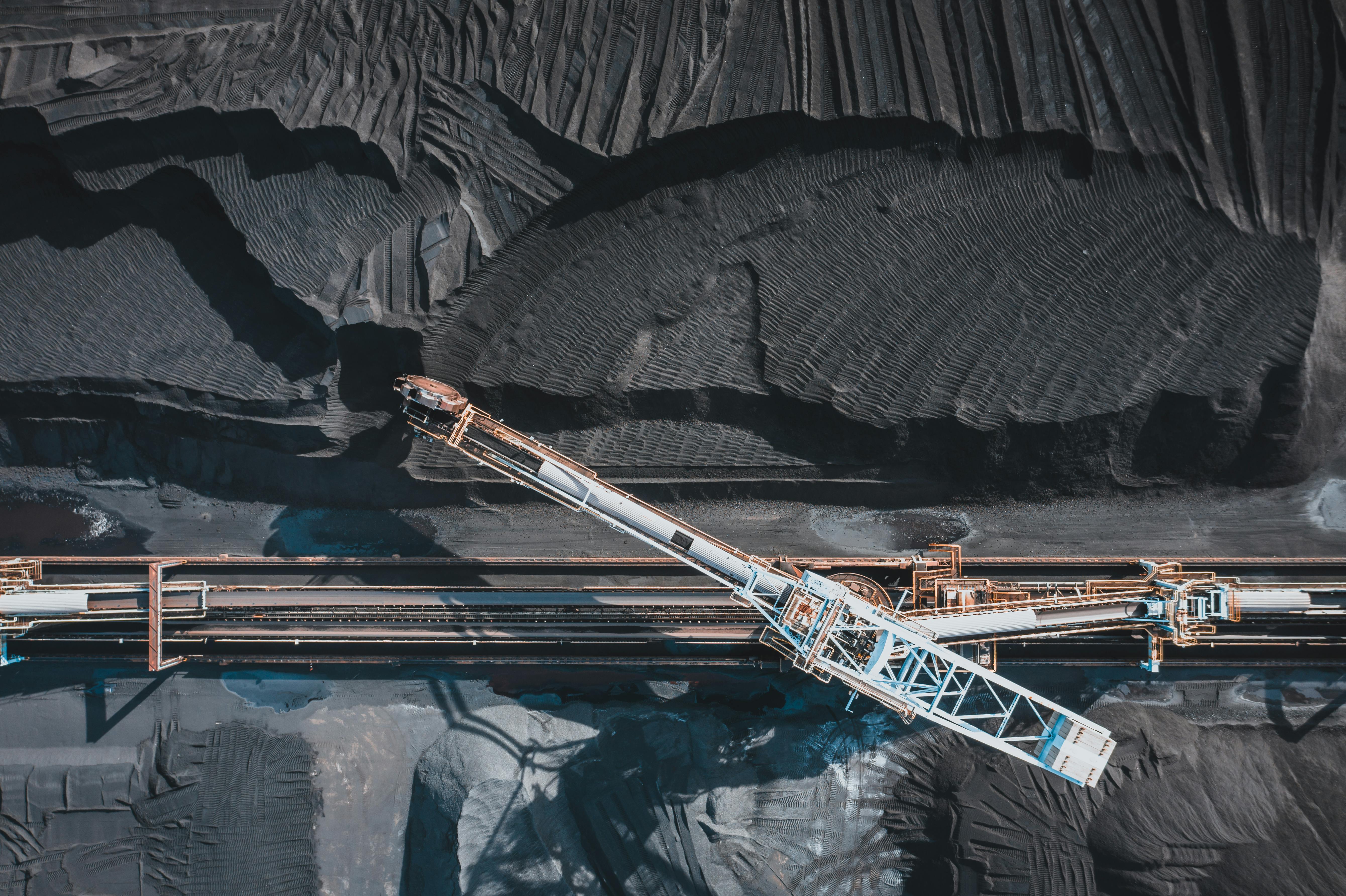 Top-down aerial view of a conveyor crossing dark commodity stockpiles