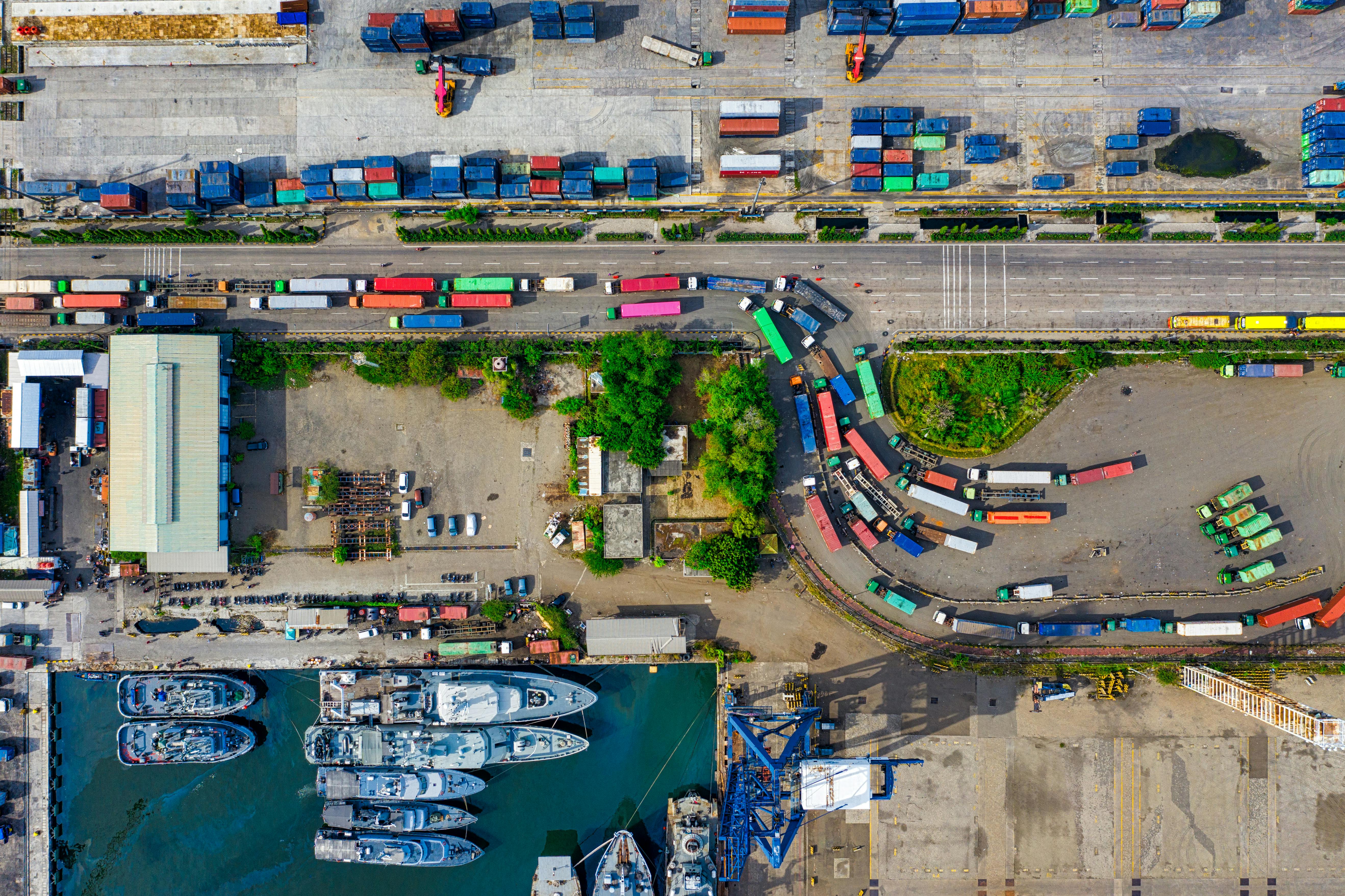 Aerial port logistics yard with trucks, containers, vessels, and route-to-market movement